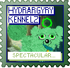 A green dog with a green octagon above their head looks at the camera against a background of a cave. The text reads 'Hydrargyry Kennelz' at the top and 'Spectacular...!' at the bottom. The stamp is green, with blue and green text.